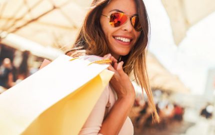 Young female adult with sunglasses and a handful of shopping bags carried over her shoulder, smiling