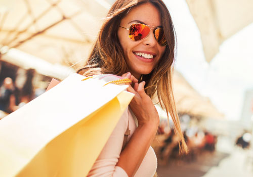 Young female adult with sunglasses and a handful of shopping bags carried over her shoulder, smiling