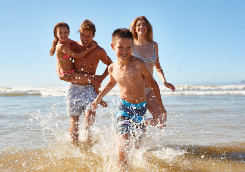 family splashing in water on beach all smiling